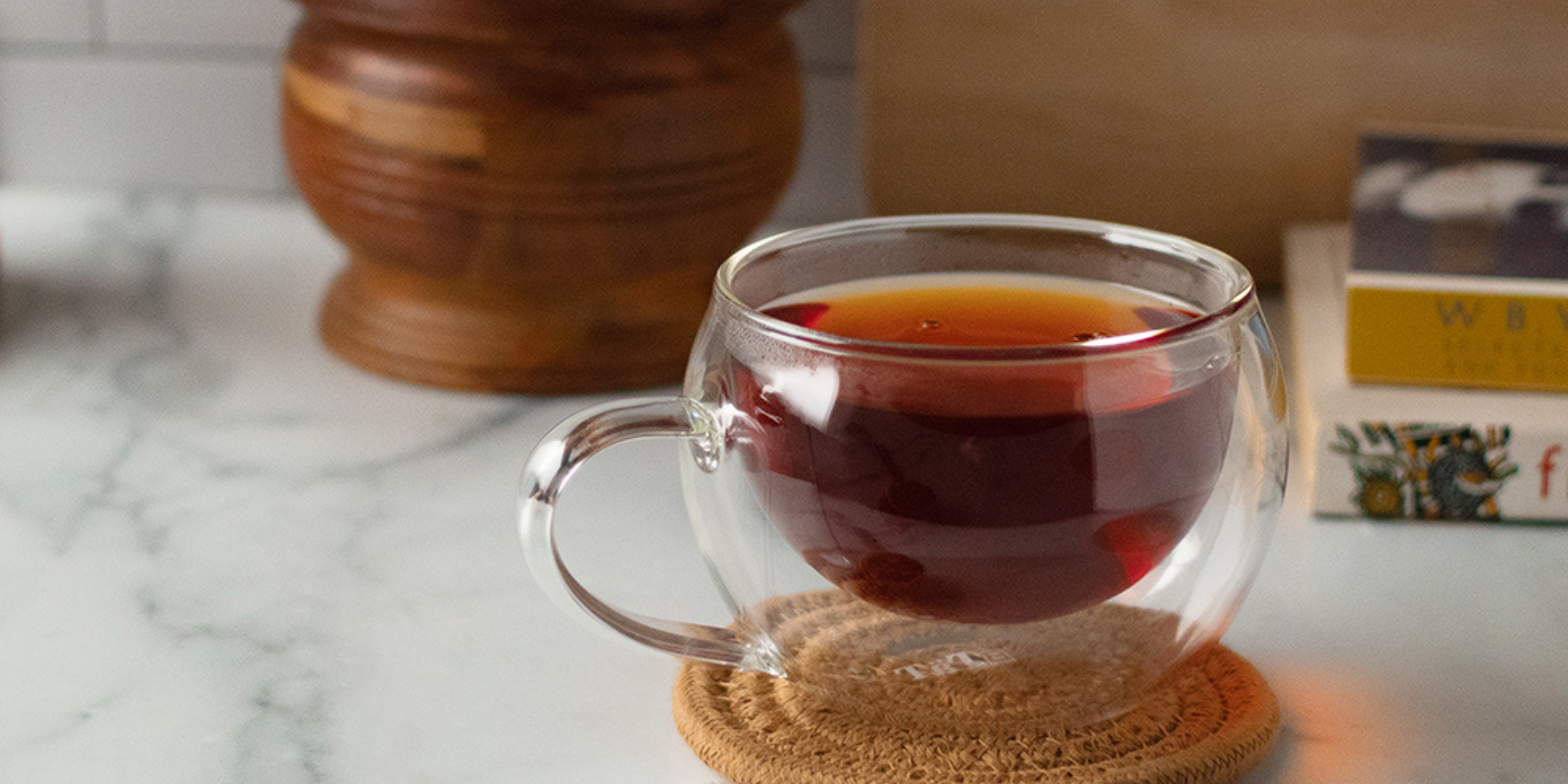 A glass cup of herbal tea sits on a woven coaster in front of some books and a mortar and pestle.