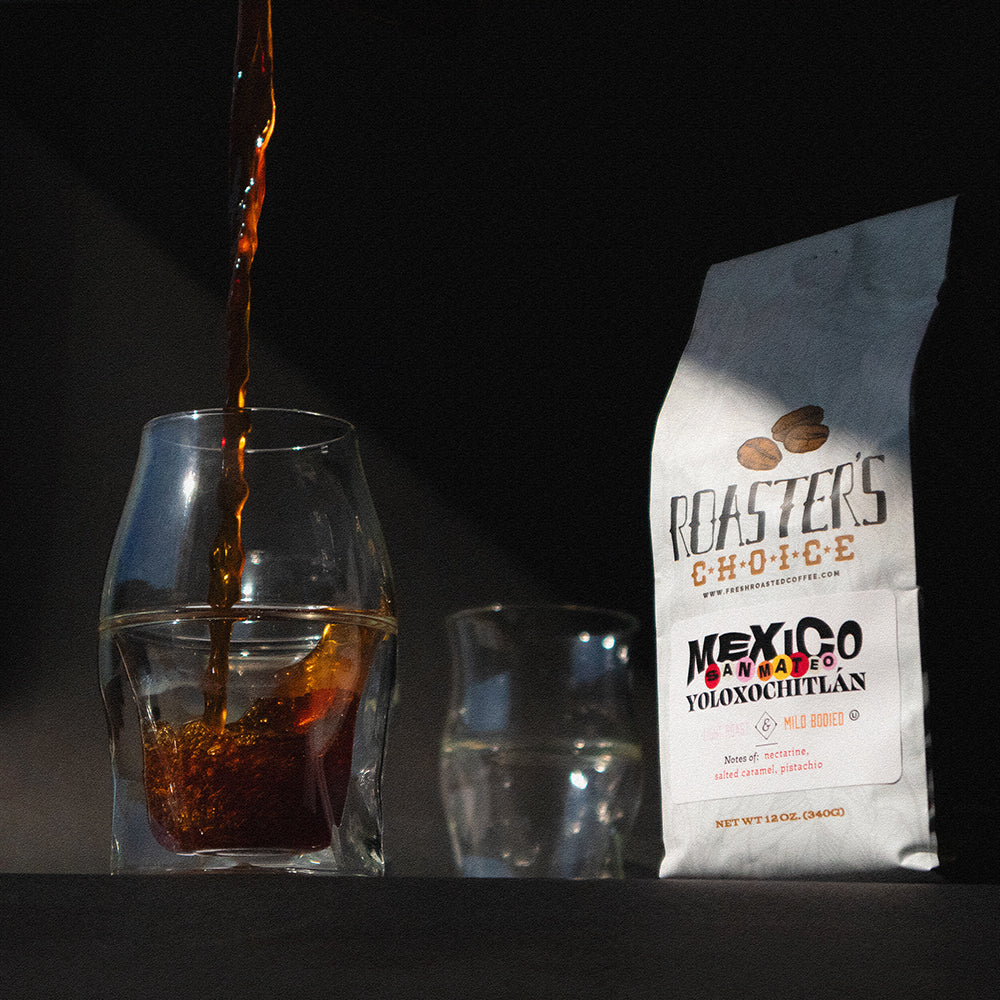 Glassware with coffee being poured into the closest glass, with a coffee bag to the side.