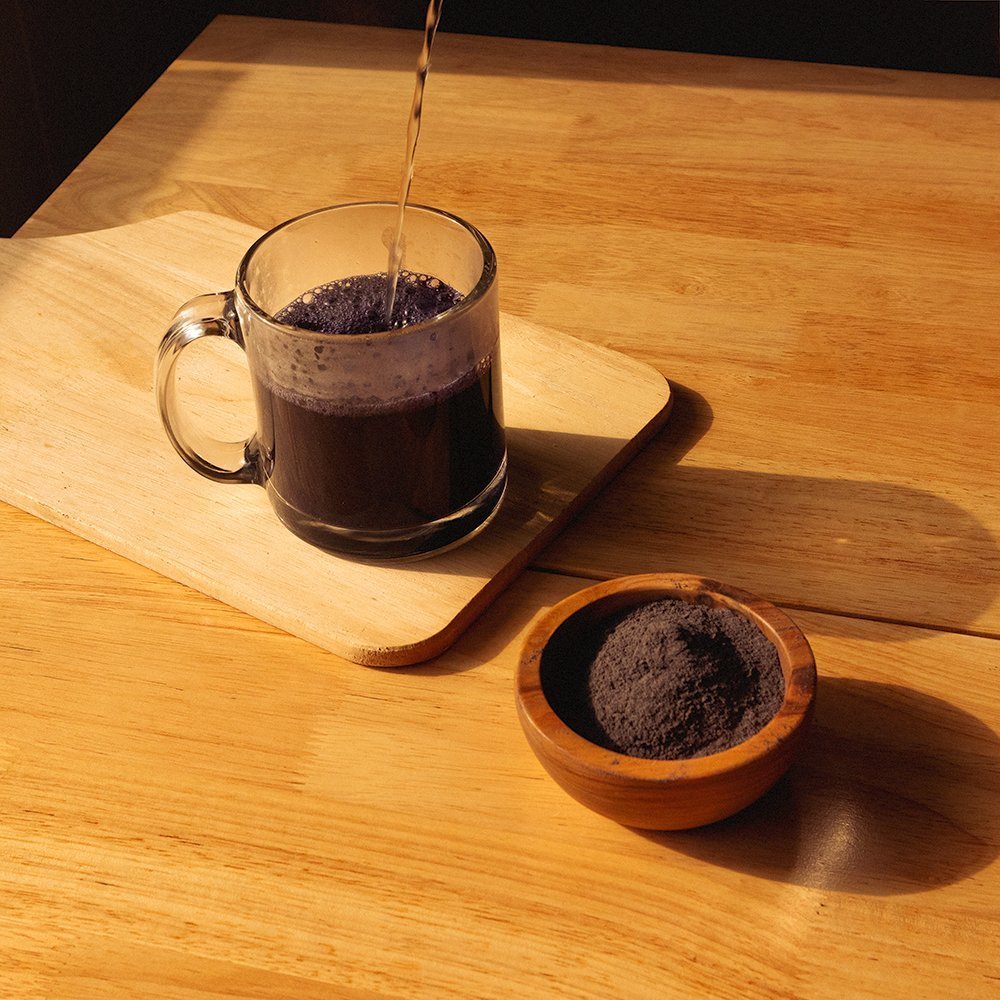 Positively Botanicals Organic Butterfly Pea Flower herbal supplement powder mixed into water, creating a deep purple infusion rich in natural plant compounds.