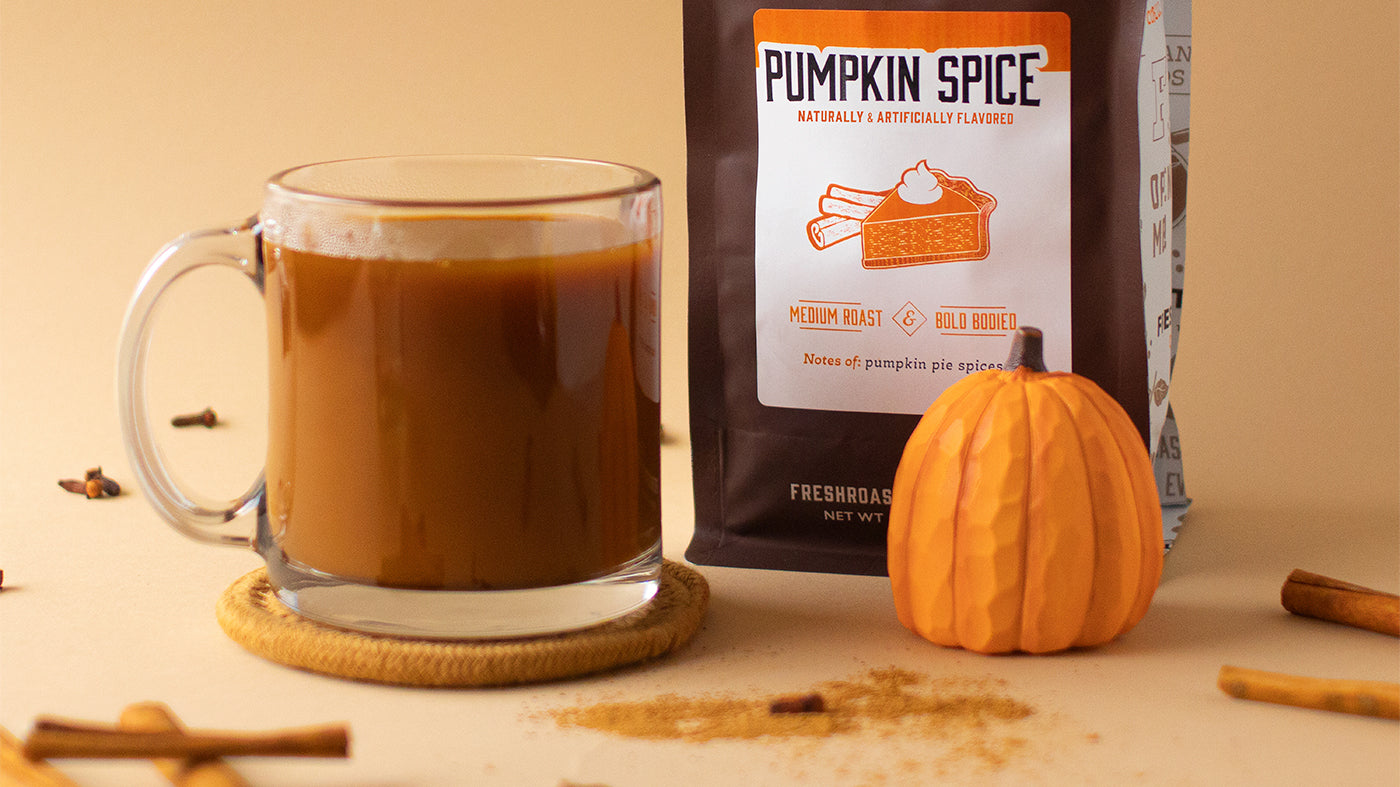 A bag of flavored Pumpkin Spice coffee behind a wooden pumpkin, a mug, and ground and stick cinnamon.