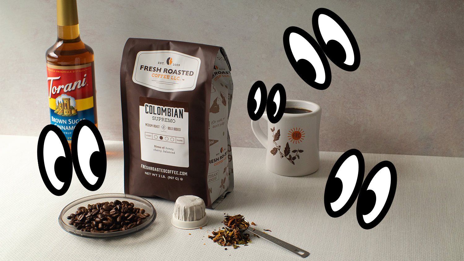 A bag of coffee, Torani syrup, mug, loose-leaf tea, and a compostable pod with illustrated eyes looking on.