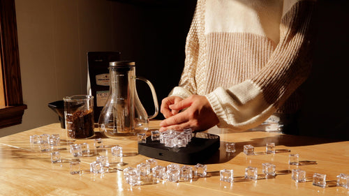 Person brushing ice cubes off a scale with a cold brewer and coffee bag in the background.