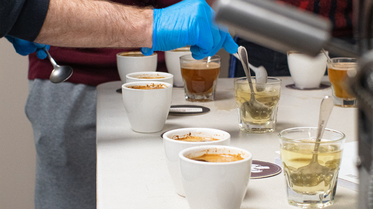 Two spoons skimming the oils and foam off the top of a cup of coffee during a cup tasting session.