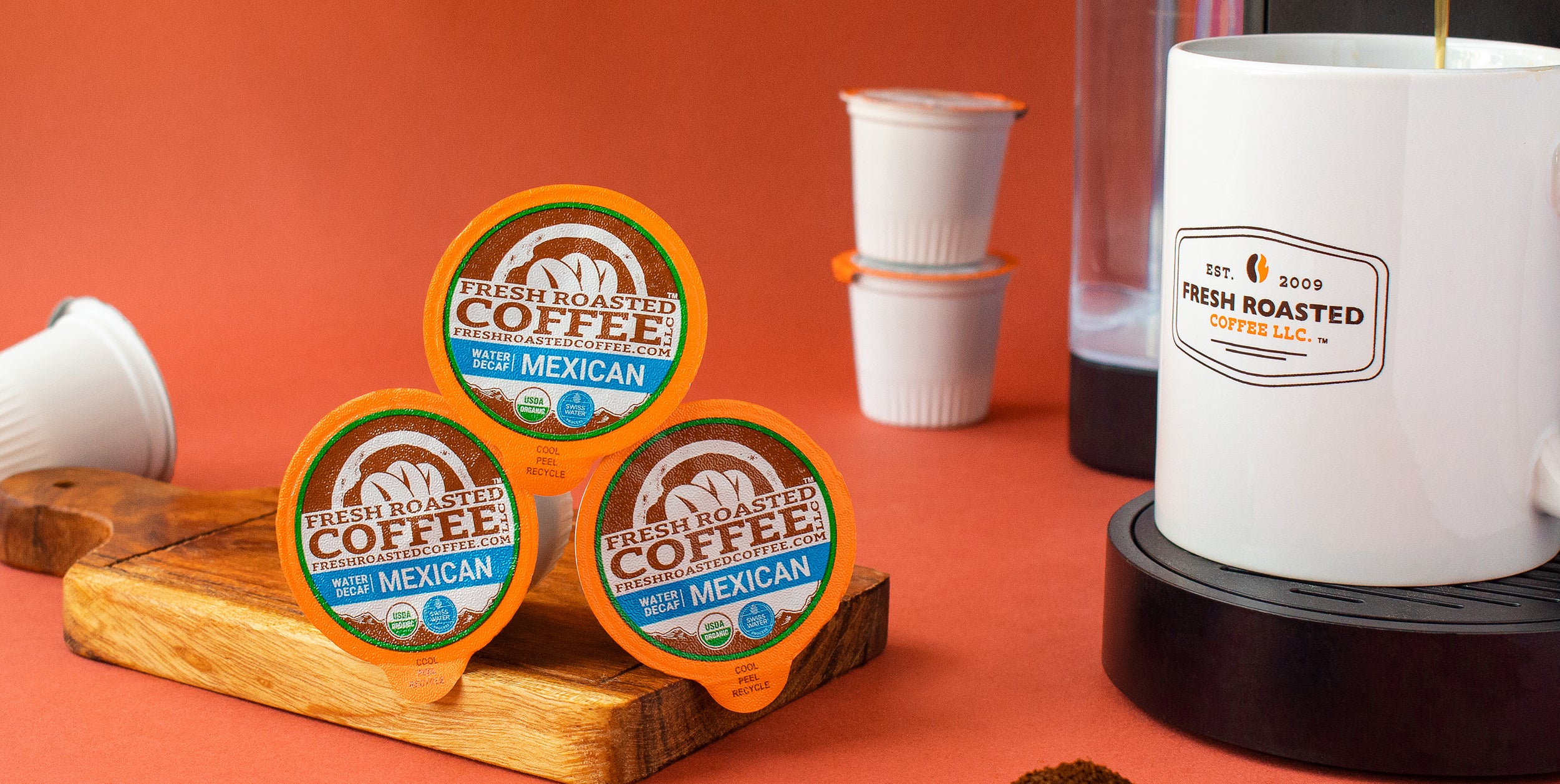 Three Organic Mexican Swiss Water Decaf pods on a serving board next to a single-serve coffee maker.