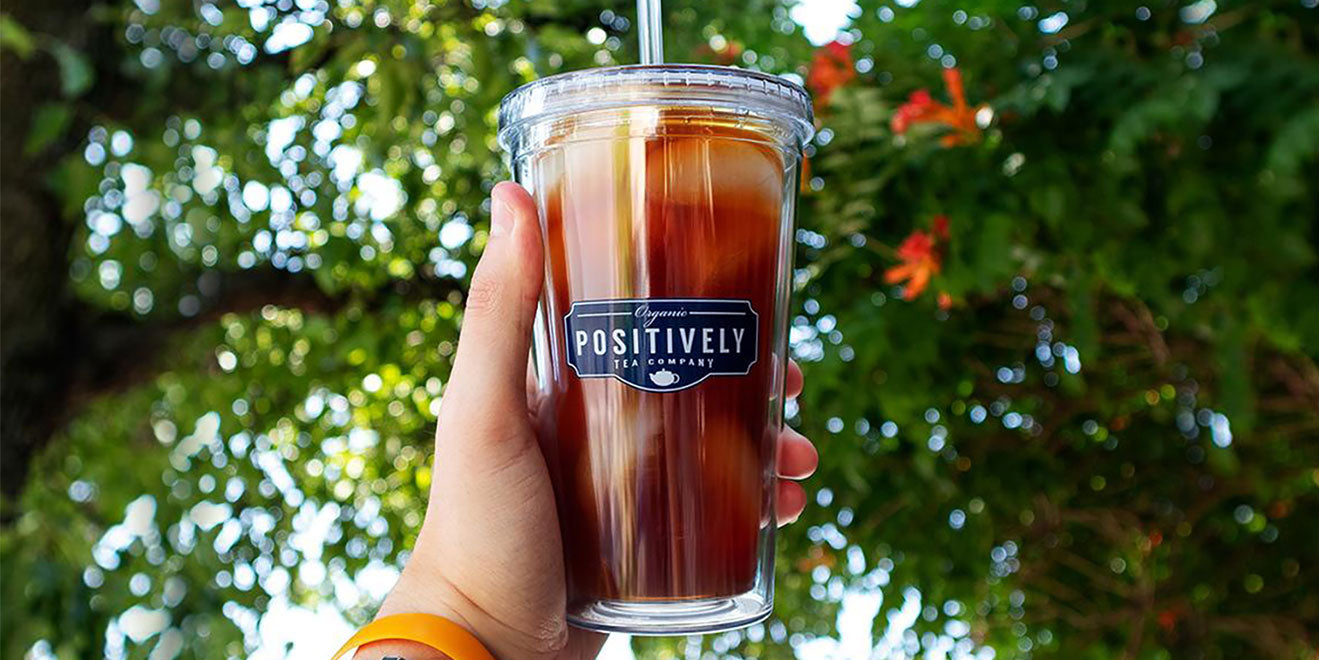 Clear tumbler of iced tea against a tree.