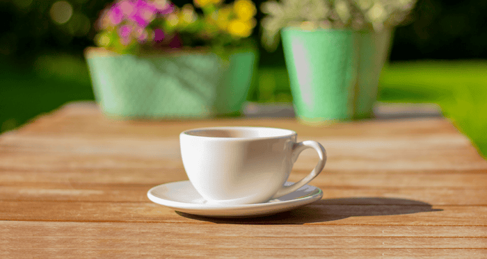 Cup of espresso sitting outside with two potted plants behind it. 