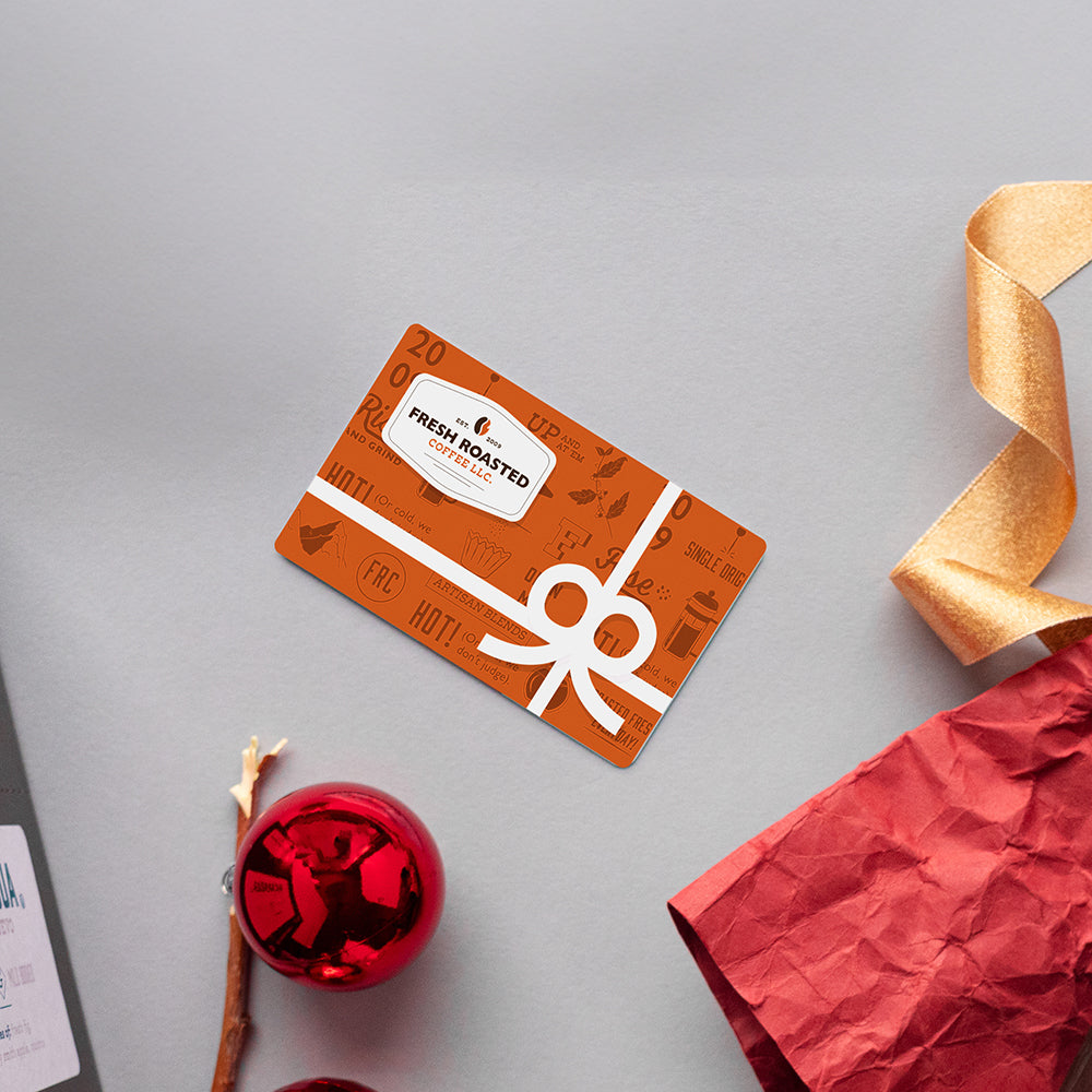 A gift card on a gray background with crinkle paper, ribbon, and an ornament around.