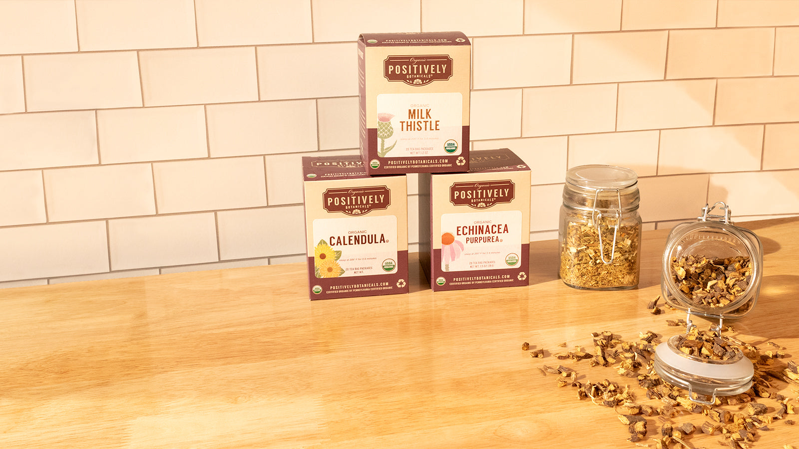 Health and wellness centered botanicals in a warm kitchen scene. 3 different boxes accompanied by 2 jars