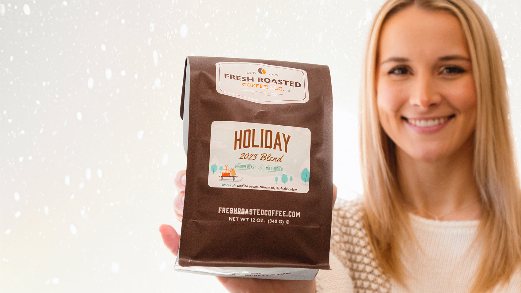 Woman smiling for real, holding a bag of coffee with snow in the background.