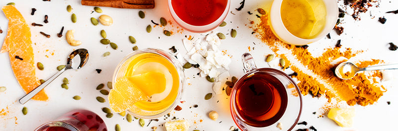 Various types of brewed teas on a white background, surrounded by various tea ingredients.