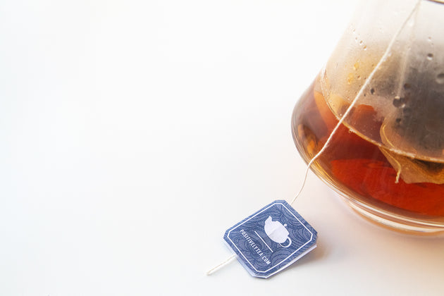 A tea bag steeping in a whiskey glass on a white background.
