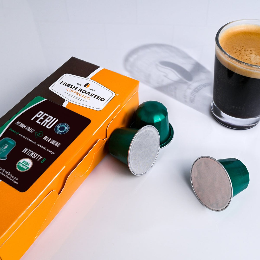Fresh Roasted Coffee Peru Organic Espresso Capsules and packaging displayed beside a rich, dark espresso shot.